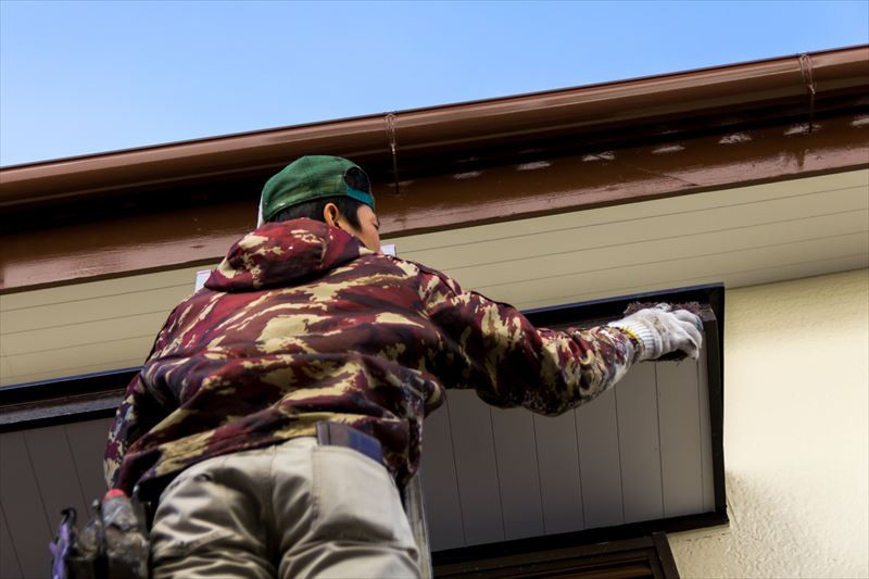 家の屋根の淵を塗る男性